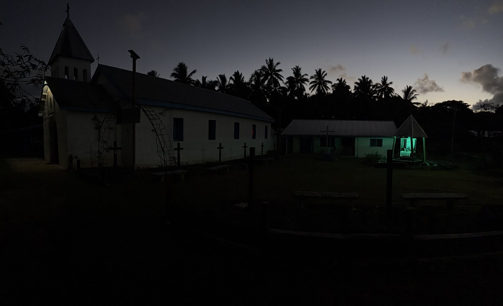 A village church at dusk, palms silhouetted against the last light